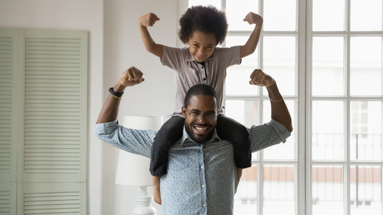 child on father's shoulders showing muscles