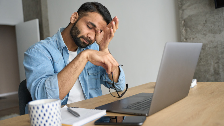 Man rubbing his eyes in front of laptop