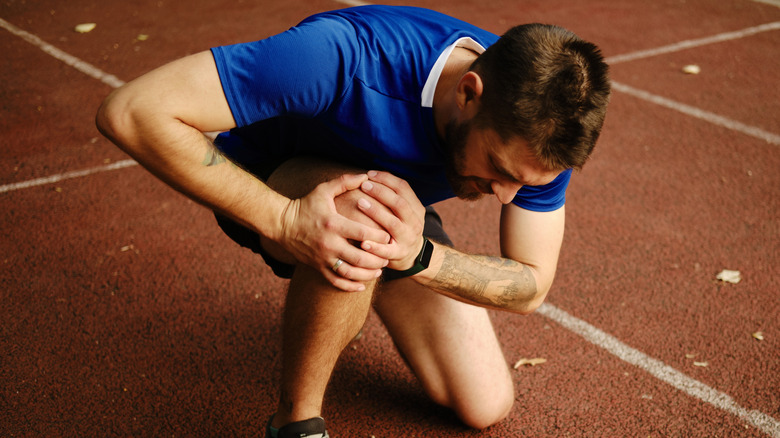 A man holding his knee while crouched on a running track