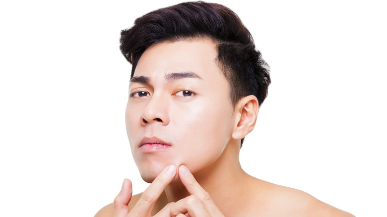 asian man picking at pimple on face