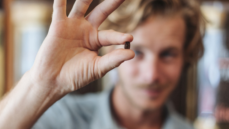 young man blurred in background holding coffee bean