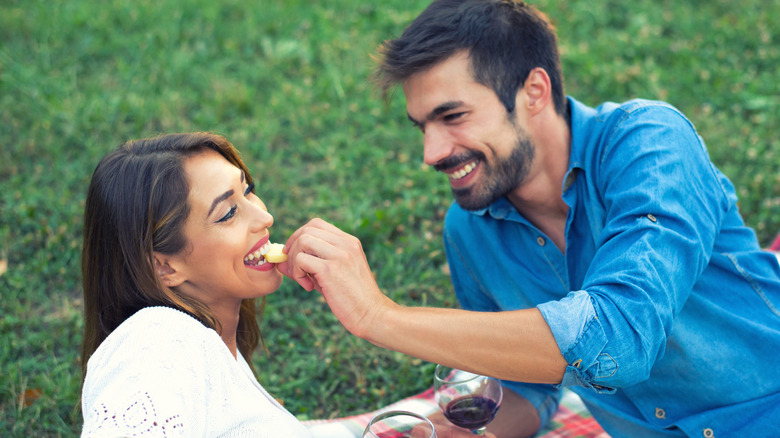 man feeding woman cheese on a picnic