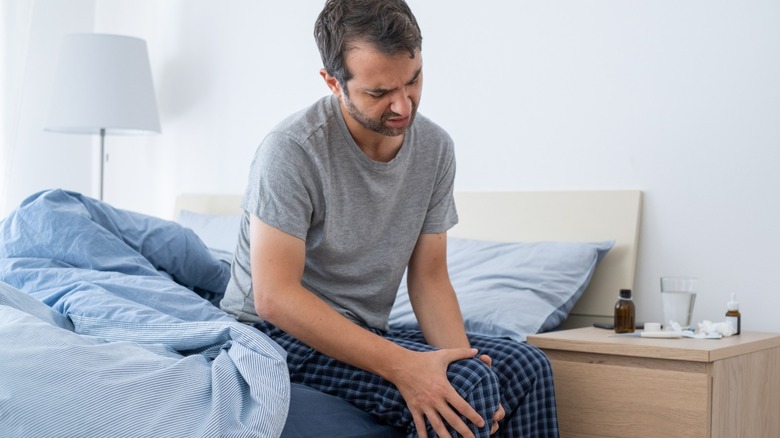 man sitting on a bed rubbing knee