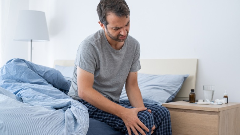 man sitting on a bed rubbing knee
