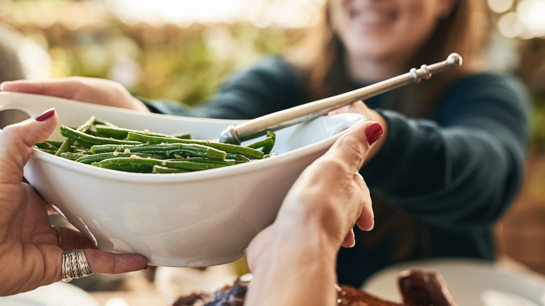 woman passing green beans to other woman at table