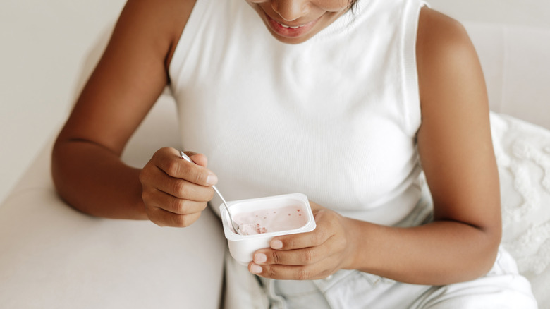 young woman eating yogurt from container at home