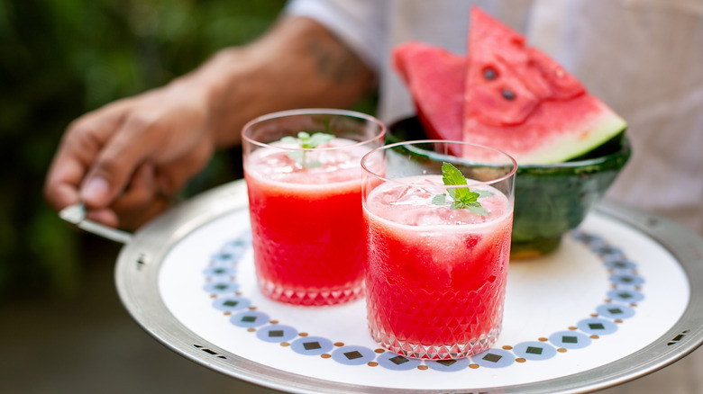 Two glasses of watermelon juice on a plate near a slice of watermelon