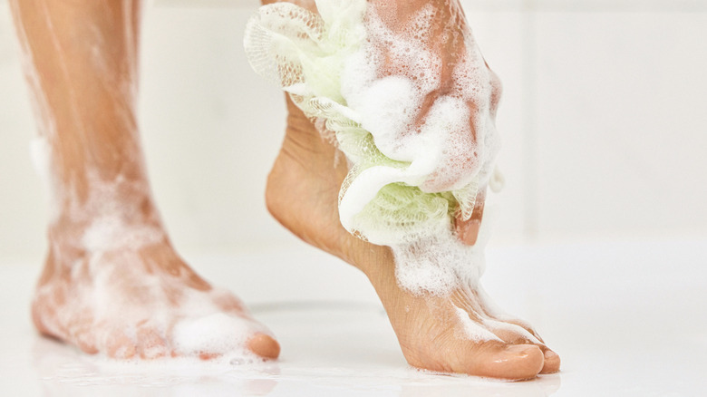 Person washing their feet in the shower with soap and a sponge