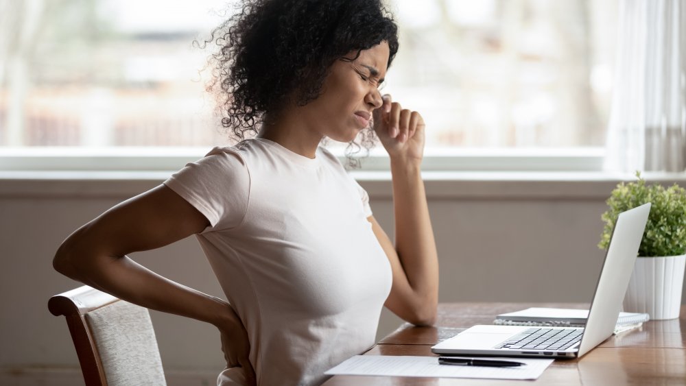 Twentysomething woman at a desk wincing from lower back pain