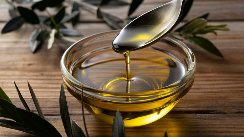 A spoon drizzling olive oil from a glass bowl on top of a wooden table