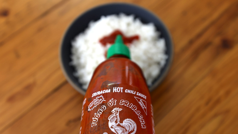 pouring sriracha on bowl of rice