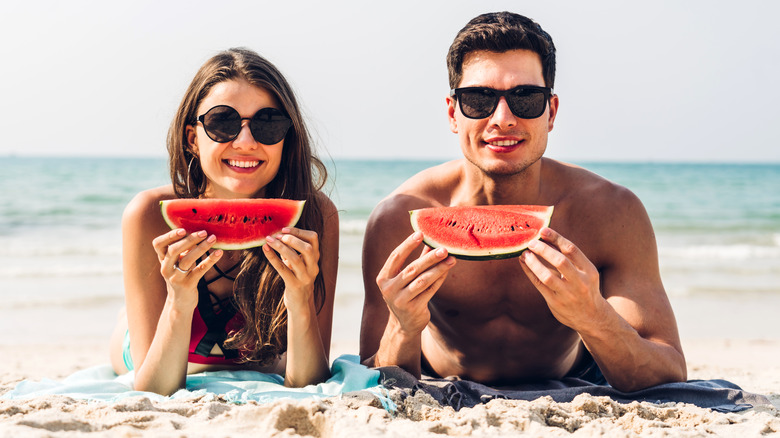 Young couple on beach holding watermelon