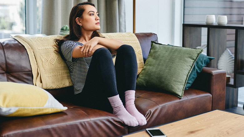 Woman with dark hair on couch staring out window