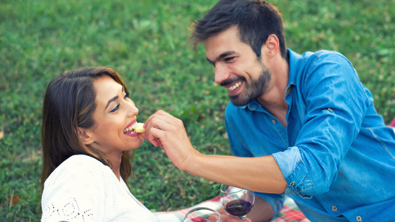 man feeding woman cheese on a picnic