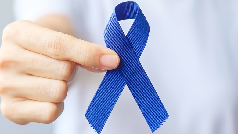 Hand holding out blue ribbon to represent colorectal cancer awareness