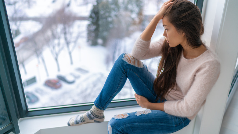 Woman sitting on windowsill staring out at snow