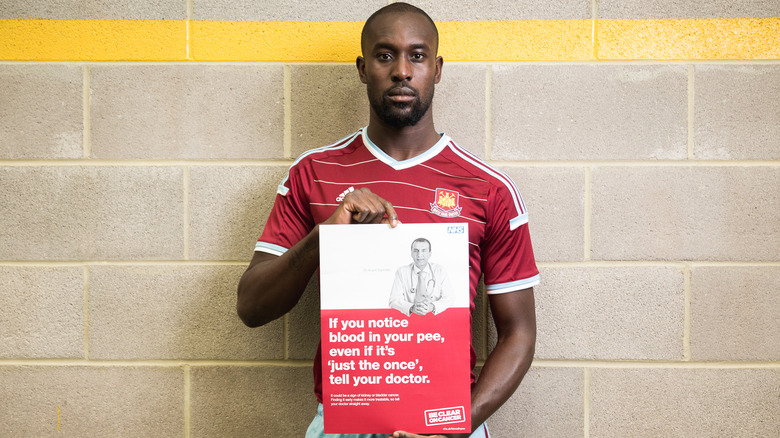 Man holding sign saying to contact your doctor if you notice blood in your pee, even if it's just once