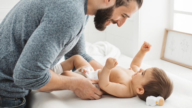 father engaging with baby while changing diaper