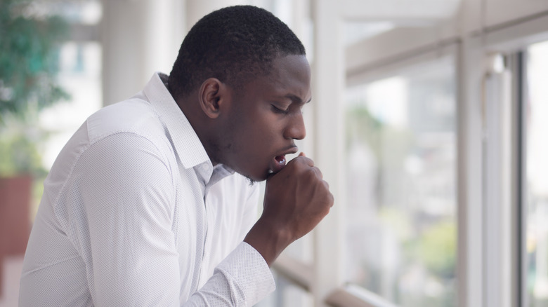 Man coughing into his hand near windows