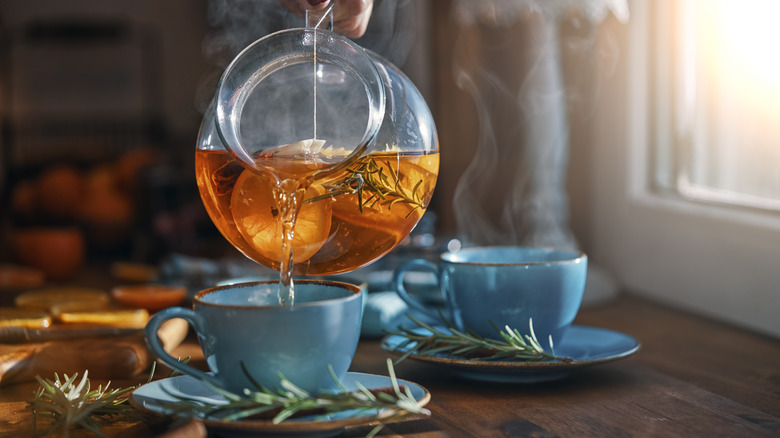 A person pouring herbal tea into a tea cup
