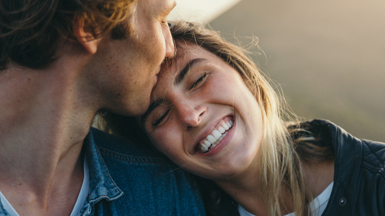 man kissing happy woman's forehead