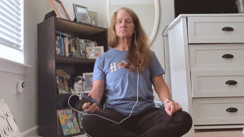A woman sitting in medication with an earpiece while holding a device