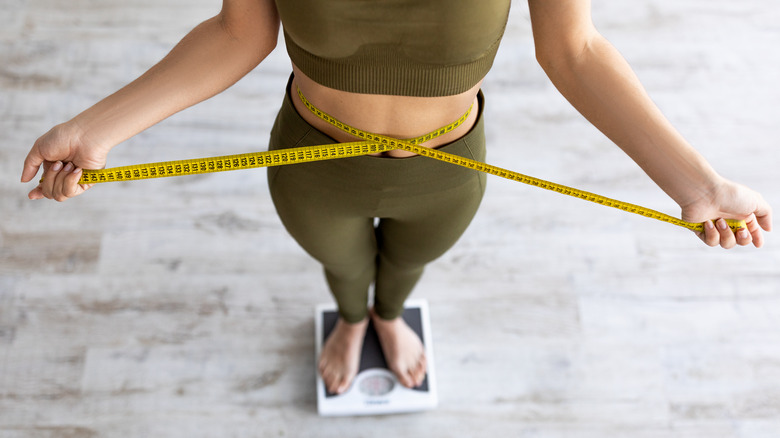 woman measuring her waist size while standing on a scale