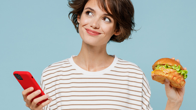 Young woman holding sandwich and phone