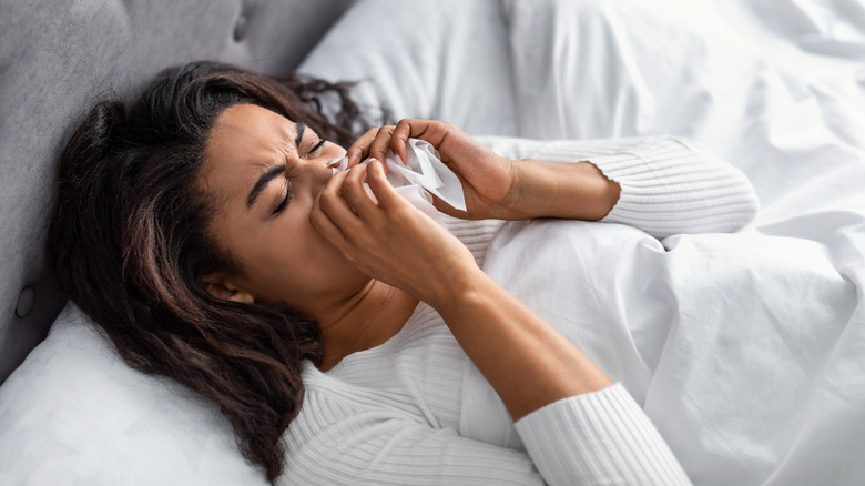 woman blowing nose in bed