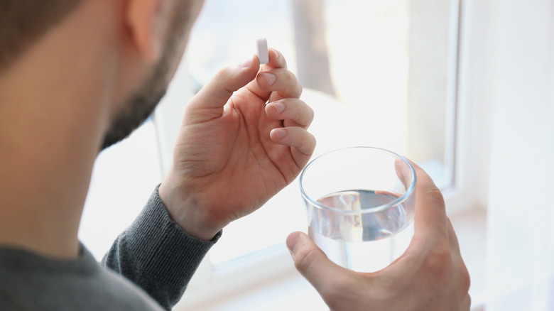 man holding medication and glass of water