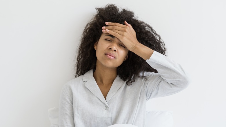 woman sitting in bed holding her hand to her headache