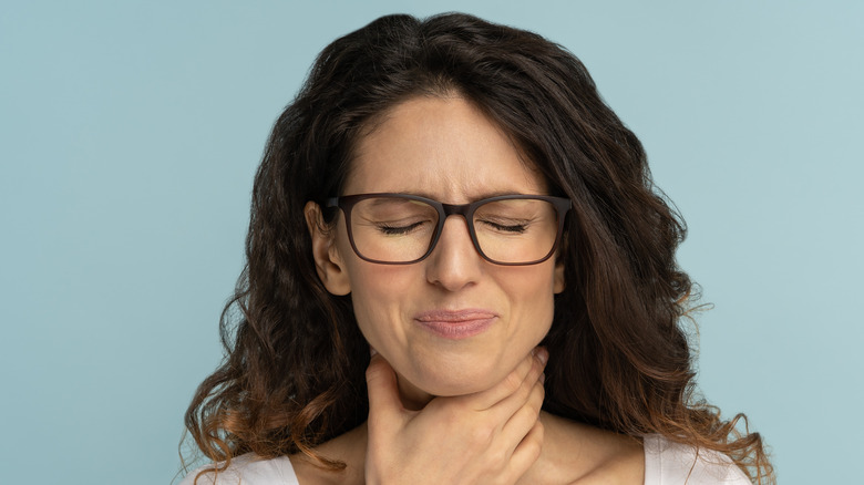 woman with glasses holding her throat in pain 