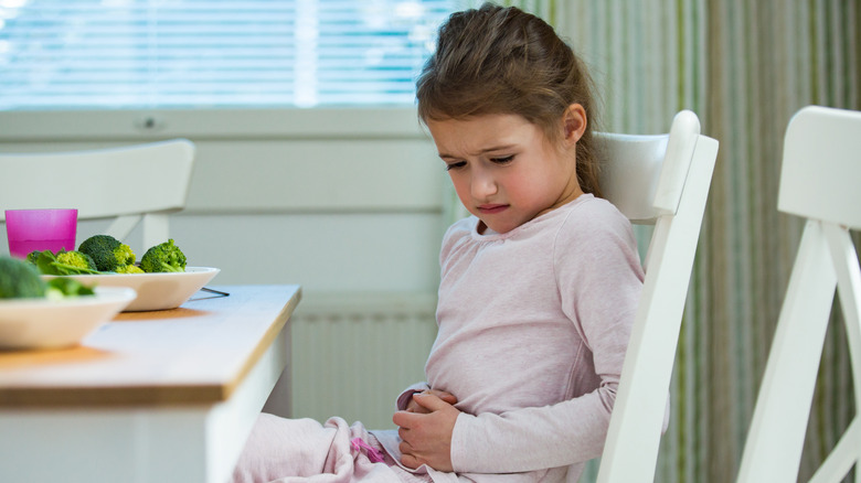 Young girl holding belly in discomfort at dinner table