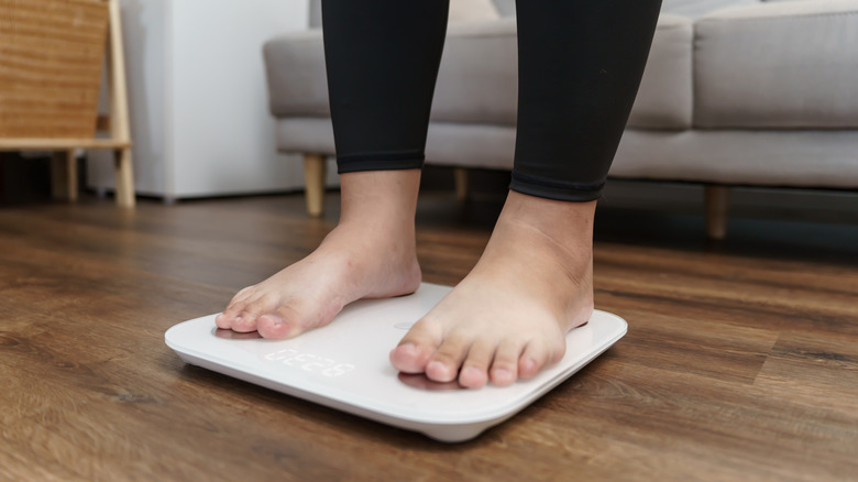 Two pale feet on a white scale in a living area.