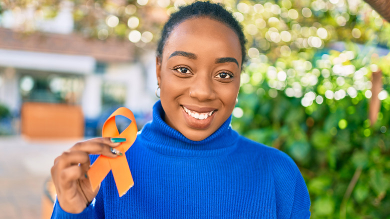 Young African American woman smiling holding orange MS awareness ribbon at the park.