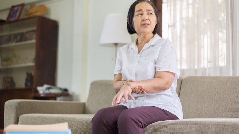 Woman with Parkinson's grasping her wrist on couch