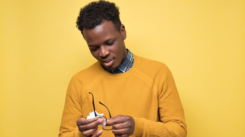 Man on yellow background using a white cloth to clean his eyeglasses