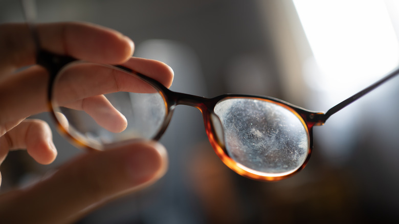 Hand holding up a pair of eyeglasses with dust and smudges on the lenses