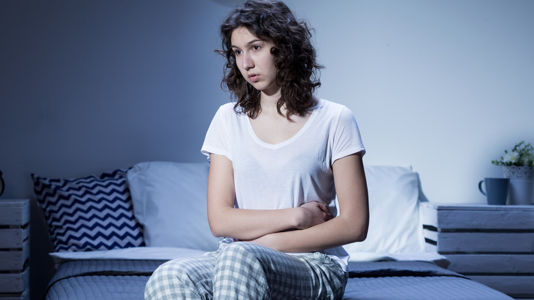 woman with bad stomach sitting on bed at night