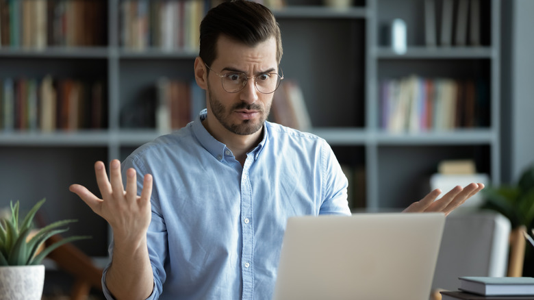 man at laptop with hands up, confused