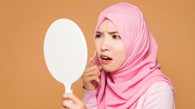 woman examining acne in mirror