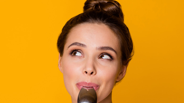 a woman with a spoon in her mouth thinking about food