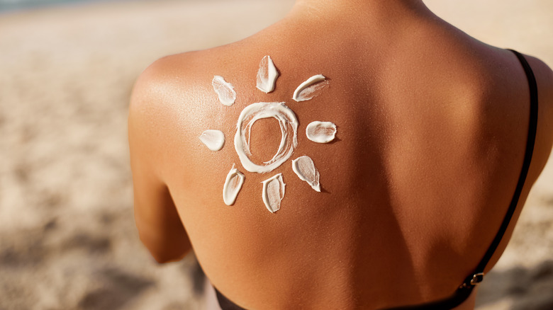 back view of a tanned woman with a sun of sunscreen on her shoulder 