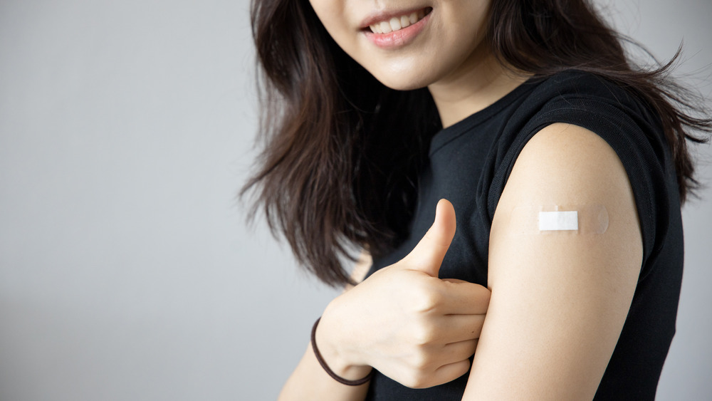 Woman with vaccine bandage giving thumbs up