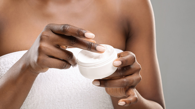 Woman dipping hands into a jar of lotion