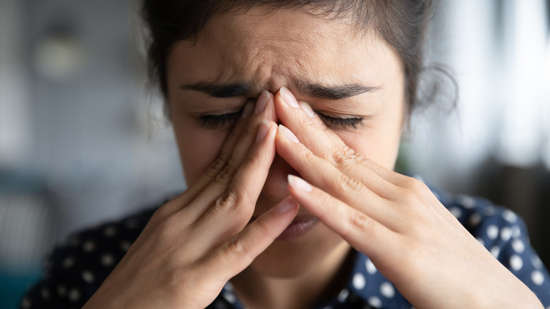 Close up of woman with her fingers at the bridge of her nose, brow furrowed in distress