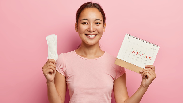 Woman holding menstrual pad and calendar