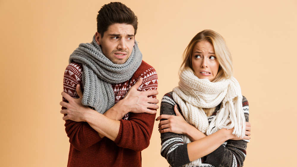 Man and woman wearing scarves and crossing their arms as if cold