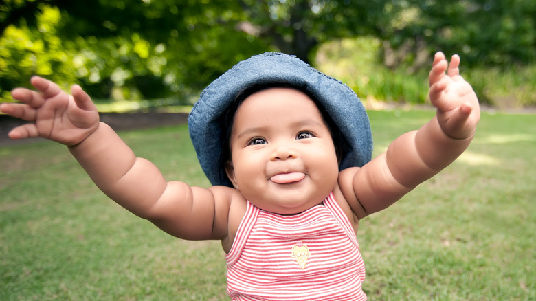 Baby sitting outdoors with arms up