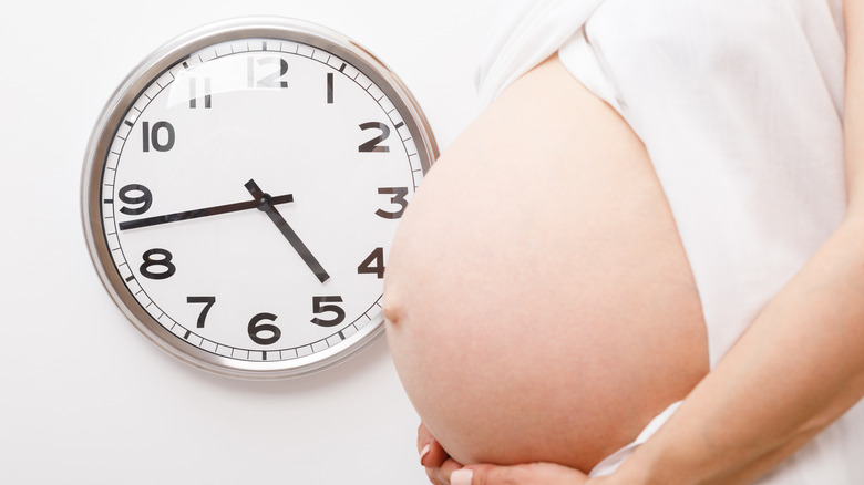 pregnant woman standing by clock